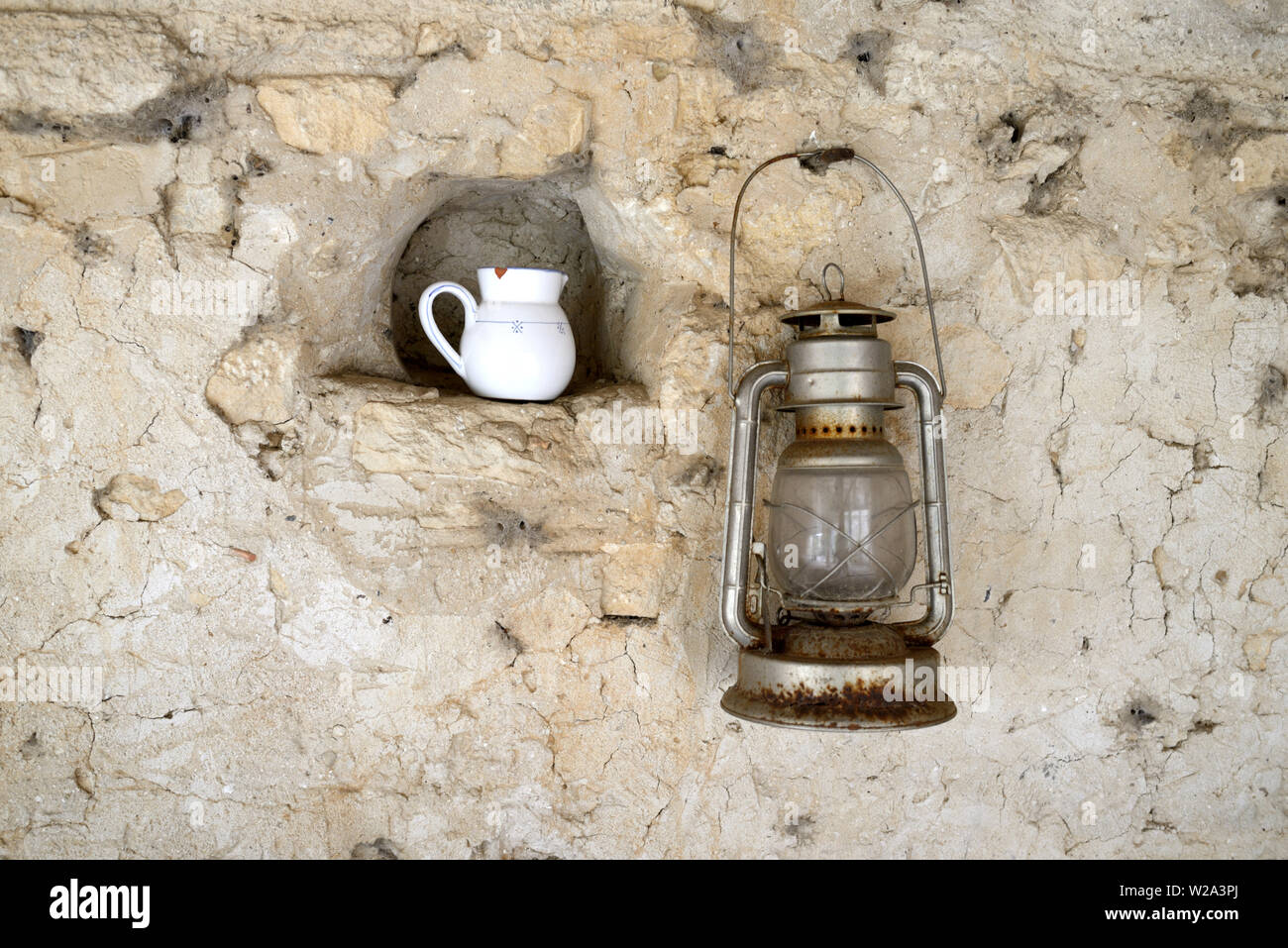Alte oder Vintage Öllampe Aufhängen an Wand- & Milchkännchen in Nische noch Leben gegen alte Steinmauer Stockfoto
