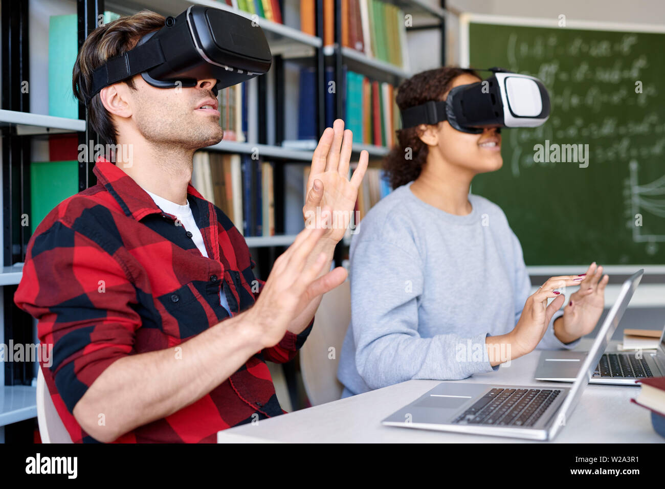 Junger Mann und seine Mitschüler im VR-Brille berühren Virtual Display Stockfoto