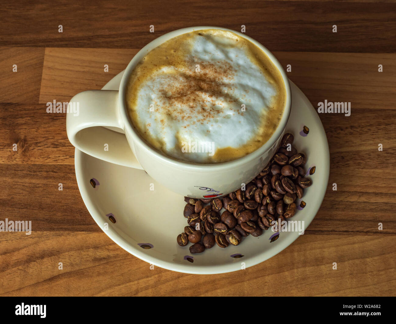 Cappuccino in eine Schale mit frisch gerösteten Kaffeebohnen auf einer hölzernen Zähler nach oben Stockfoto