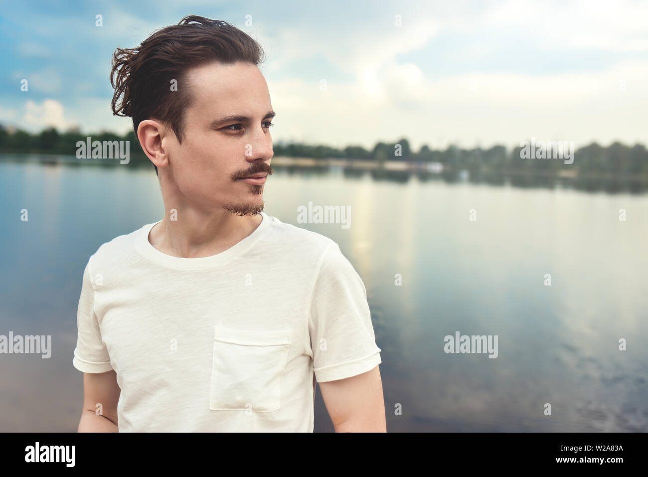 Portrait des jungen Mannes geniesst man eine wunderschöne Aussicht und in die Ferne schaut in der Nähe von einem See und Wald. Sommer. Feder. Natur Stockfoto