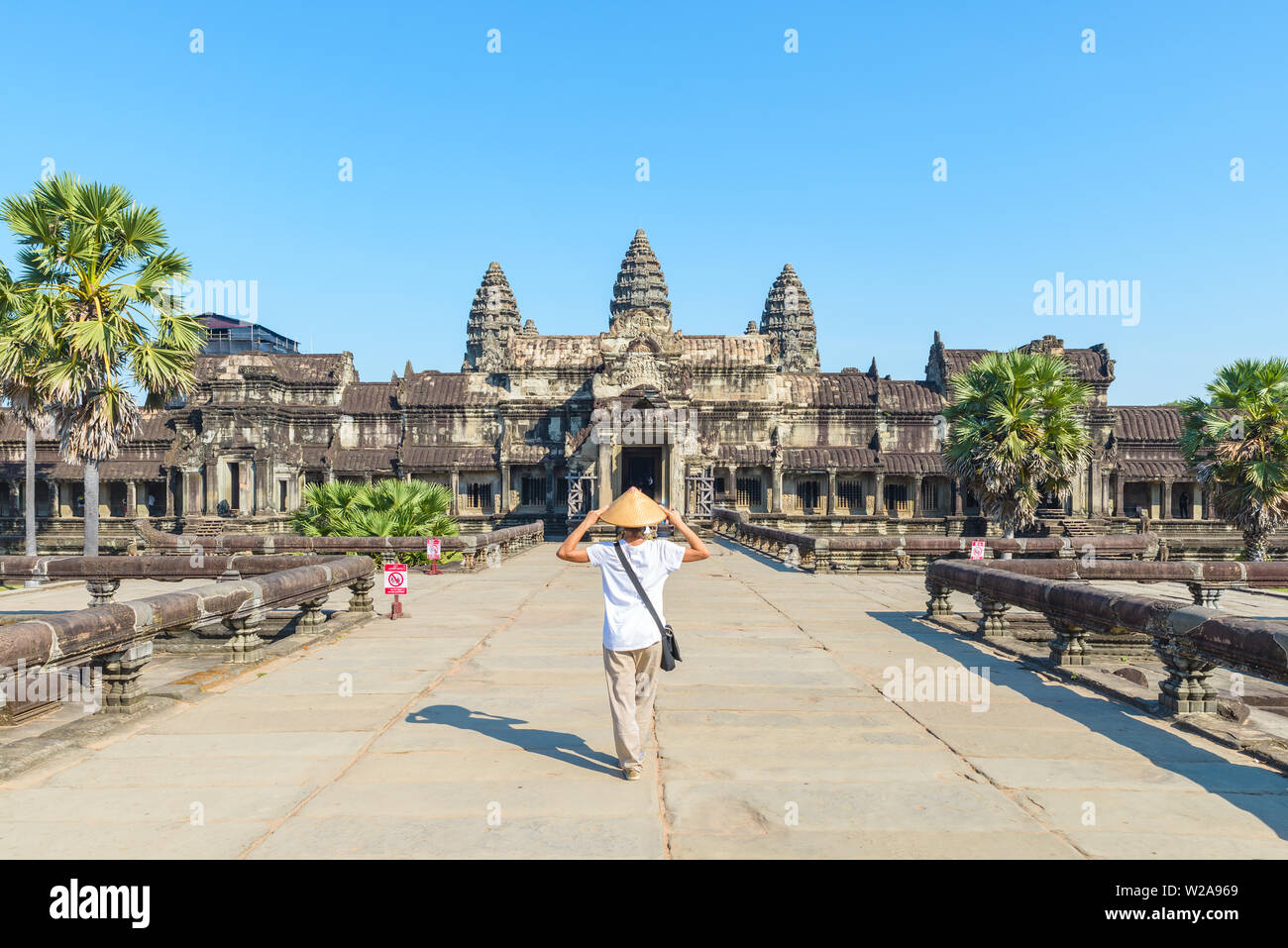 Eine touristische besuchen die Ruinen von Angkor Wat bei Sonnenaufgang, Reiseziel Kambodscha. Frau mit traditionellen Hut und erhobenen Armen, Rückansicht, Hauptfassade und Stockfoto