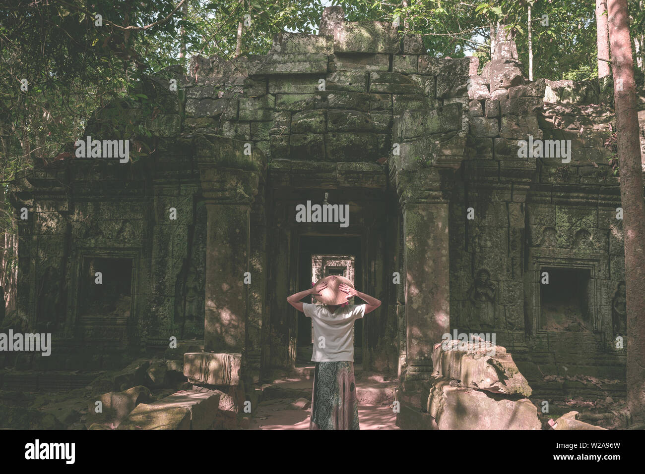 Eine touristische besuchen Angkor Ruinen inmitten Dschungel, Tempelanlage Angkor Wat, Reiseziel Kambodscha. Frau mit traditionellen Hut, Ansicht von hinten. Stockfoto