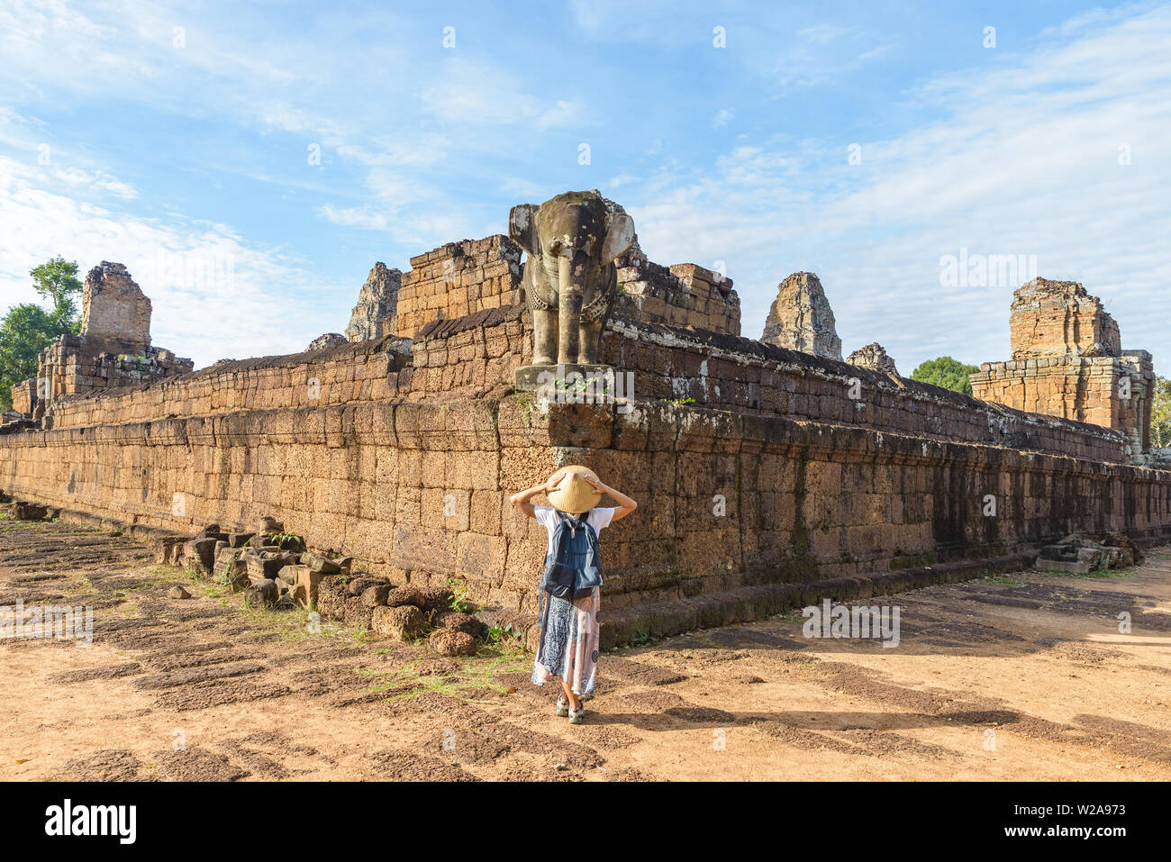 Eine touristische besuchen die Ruinen von Angkor Wat bei Sonnenaufgang, Pre Rup Tempel, Reiseziel Kambodscha. Frau mit traditionellen Hut und erhobenen Armen, Rückansicht, Stockfoto
