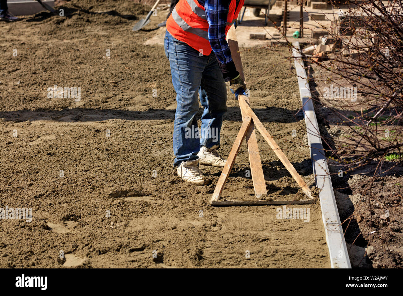 Der Arbeitnehmer richtet die Keller mit einem Holz- Ebene beginnen zu verlegen Pflastersteine auf die Fußgängerzone. Stockfoto