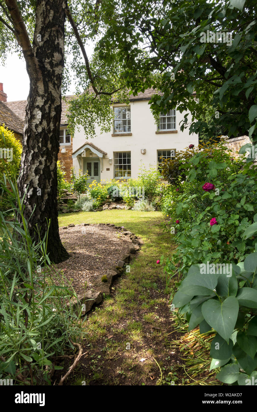 Attraktive alte Creme lackiert Haus mit Schiebefenstern und eine Veranda mit einem schönen gepflegten Garten mit Bäumen, Pflanzen und Pfad, Uppingham England, Großbritannien Stockfoto