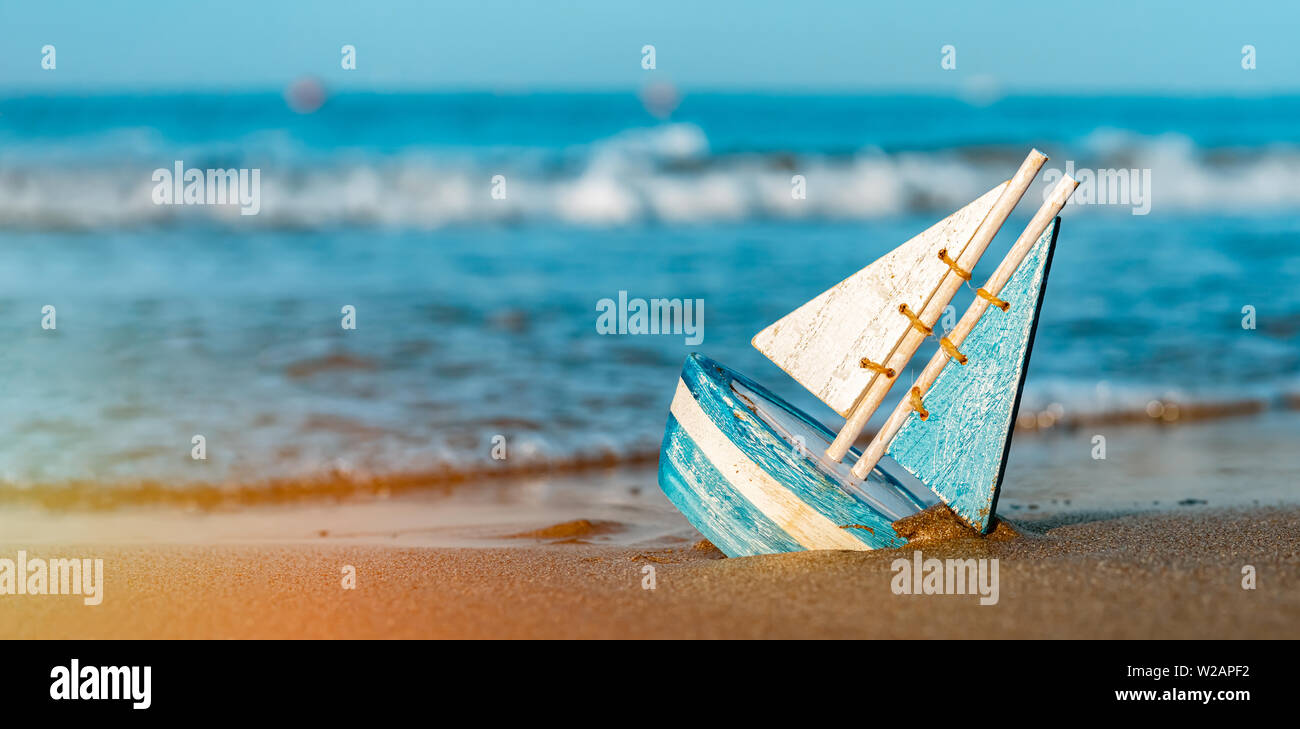 Holzspielzeug Segelboot begraben in Sand in der Nähe der Küste im Sommer. Urlaub und Freizeit Konzept Konzept. Stockfoto