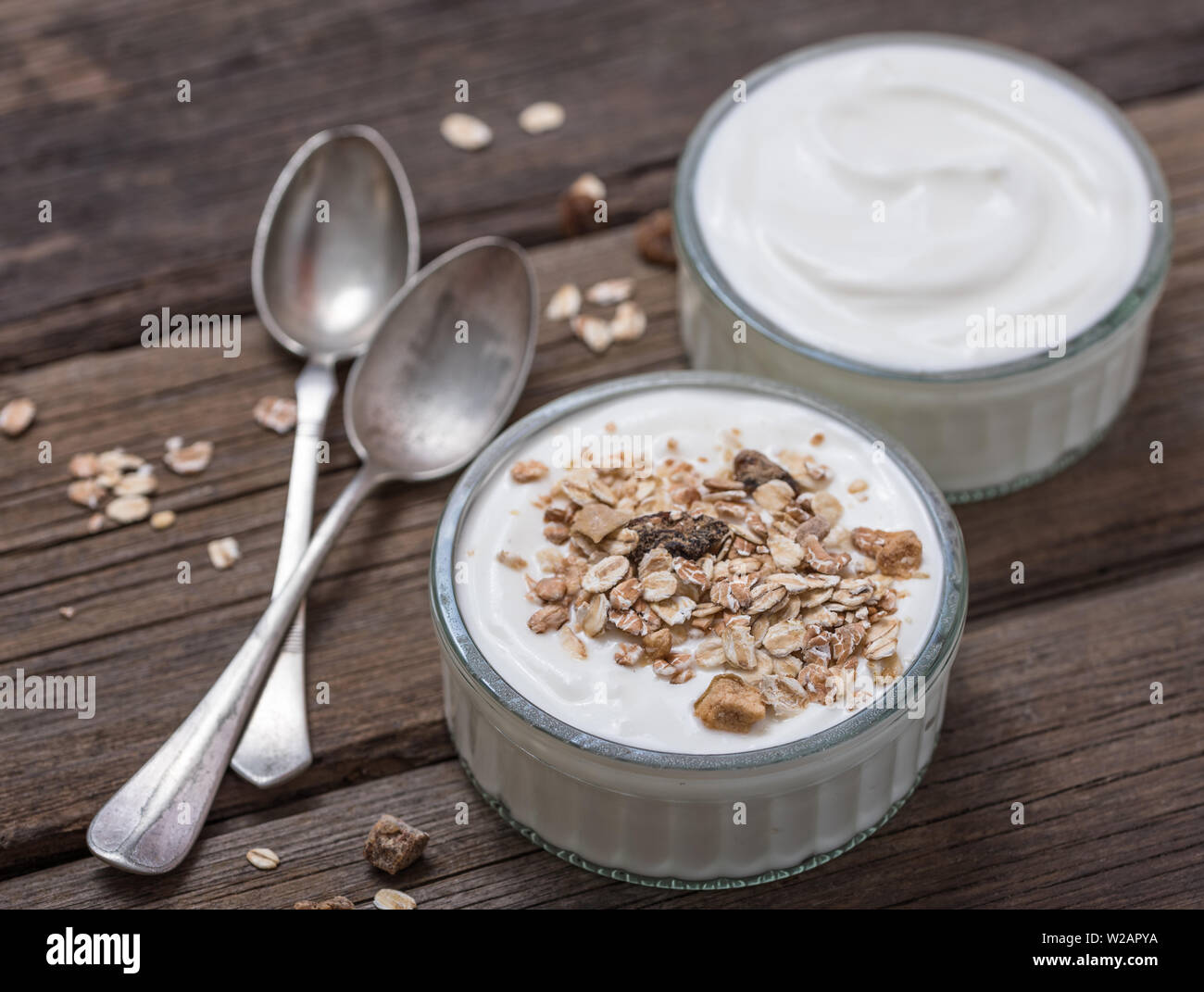 Weißer Joghurt im Glas Schale mit Haferflocken oben auf rustikalen Holztisch. Stockfoto