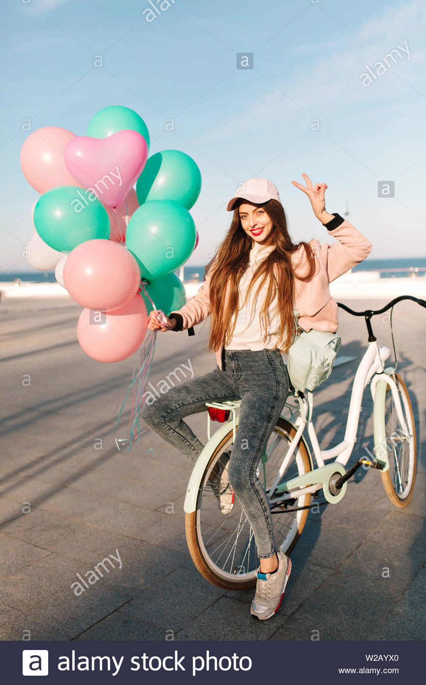 In voller Länge Porträt der schlanke Mädchen in Gap und trendigen Sneakers  sitzen auf dem Fahrrad