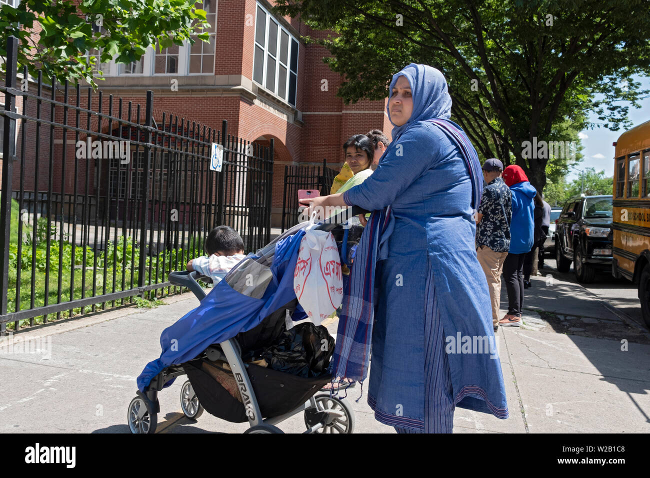 Eine muslimische Frau in einem Hijab und ethnische Kleidung wartet auf ihr Kind außerhalb einer Schule, PS 69, in Jackson Heights, Queens, New York City. Stockfoto