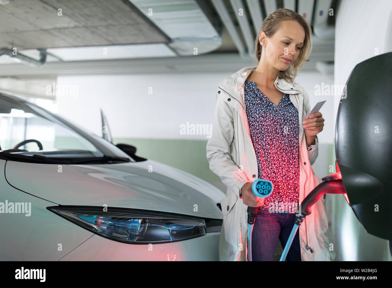 Junge Frau laden ein elektrisches Fahrzeug in einer Tiefgarage mit e-Auto Ladegerät ausgestattet. Car Sharing-Konzept. Stockfoto