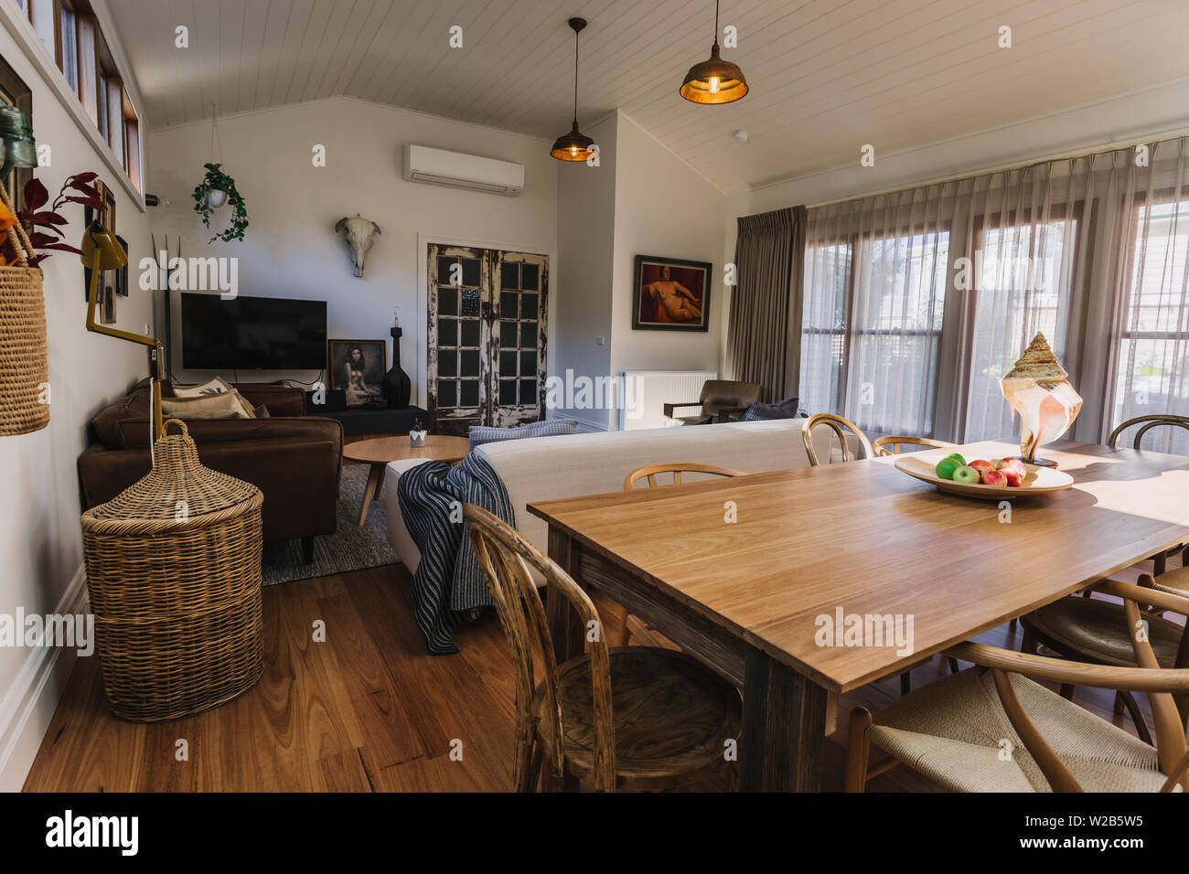 Ess- und Wohnbereich mit gewölbten Holz Öffnen gesäumt Decken und großen Fenstern mit Vorhängen und Bettwäsche Stockfoto