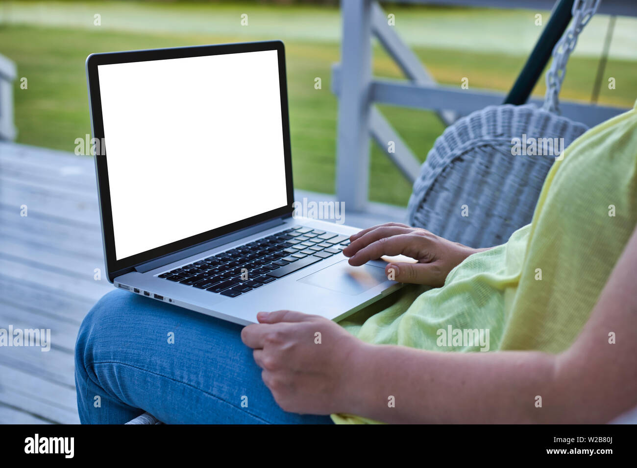 Frau mit Laptop auf dem Deck mit einem Schwingen in einer ländlichen Gegend. Die Frau trägt Gelb. Der Fokus ist selektive Bereitstellung Copyspace. Stockfoto