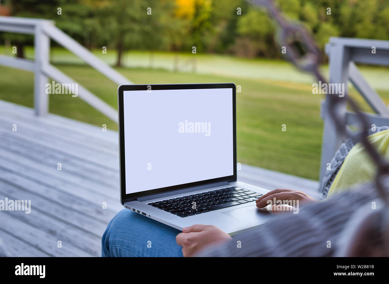 Frau mit Laptop auf dem Deck mit einem Schwingen in einer ländlichen Gegend. Die Frau trägt Gelb. Der Fokus ist selektive Bereitstellung Copyspace. Stockfoto