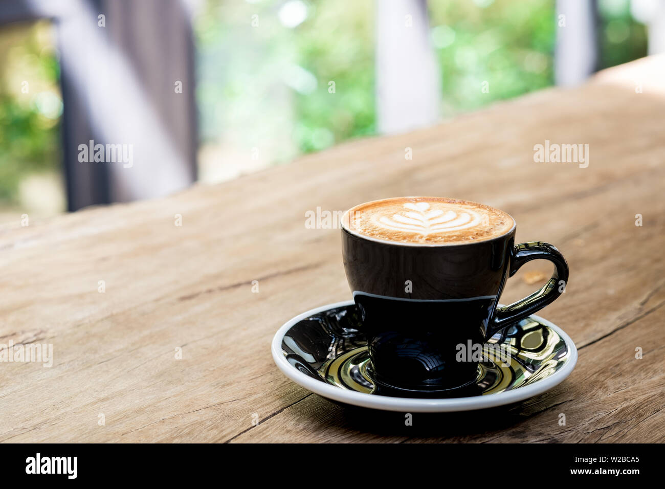 Heißen Cappuccino Tasse mit Baum latte Art Milch Schaum auf Holz Tisch am Fenster, im Garten in der Sonne im Cafe Restaurant. Freizeit Lifestyle. foo Stockfoto