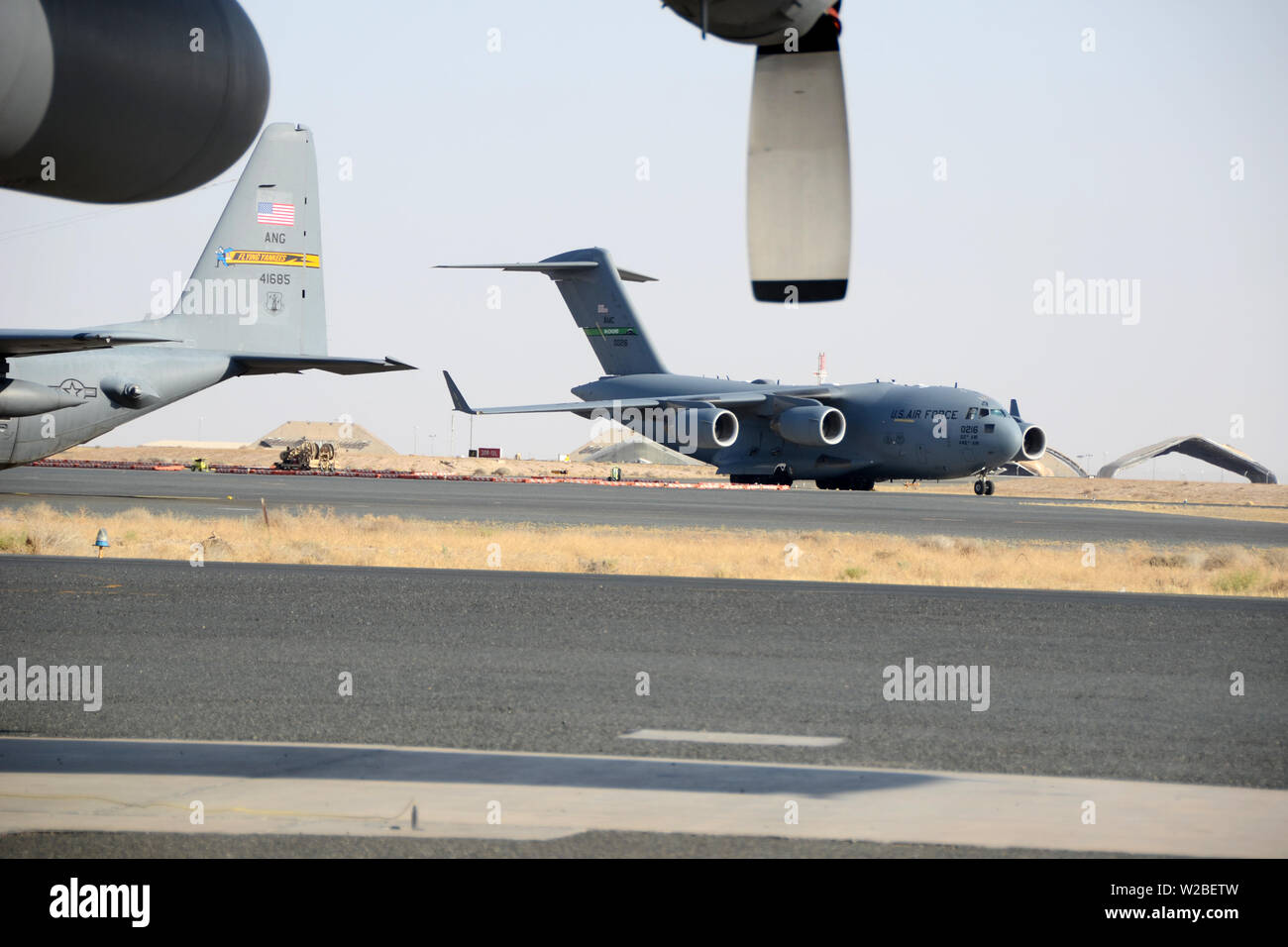 Eine C-17 Globus Master III Taxis vorbei an einer C-130 Hercules im Ali Al Salem Air Base, Kuwait, 3. Juli 2019. Die Einheiten sind derzeit hier zum Einsatz mit taktischer Lufttransport zur zentralen Befehl Verantwortungsbereich. (U.S. Air National Guard Foto vom Kapitän Stephen Hudson/Freigegeben) Stockfoto