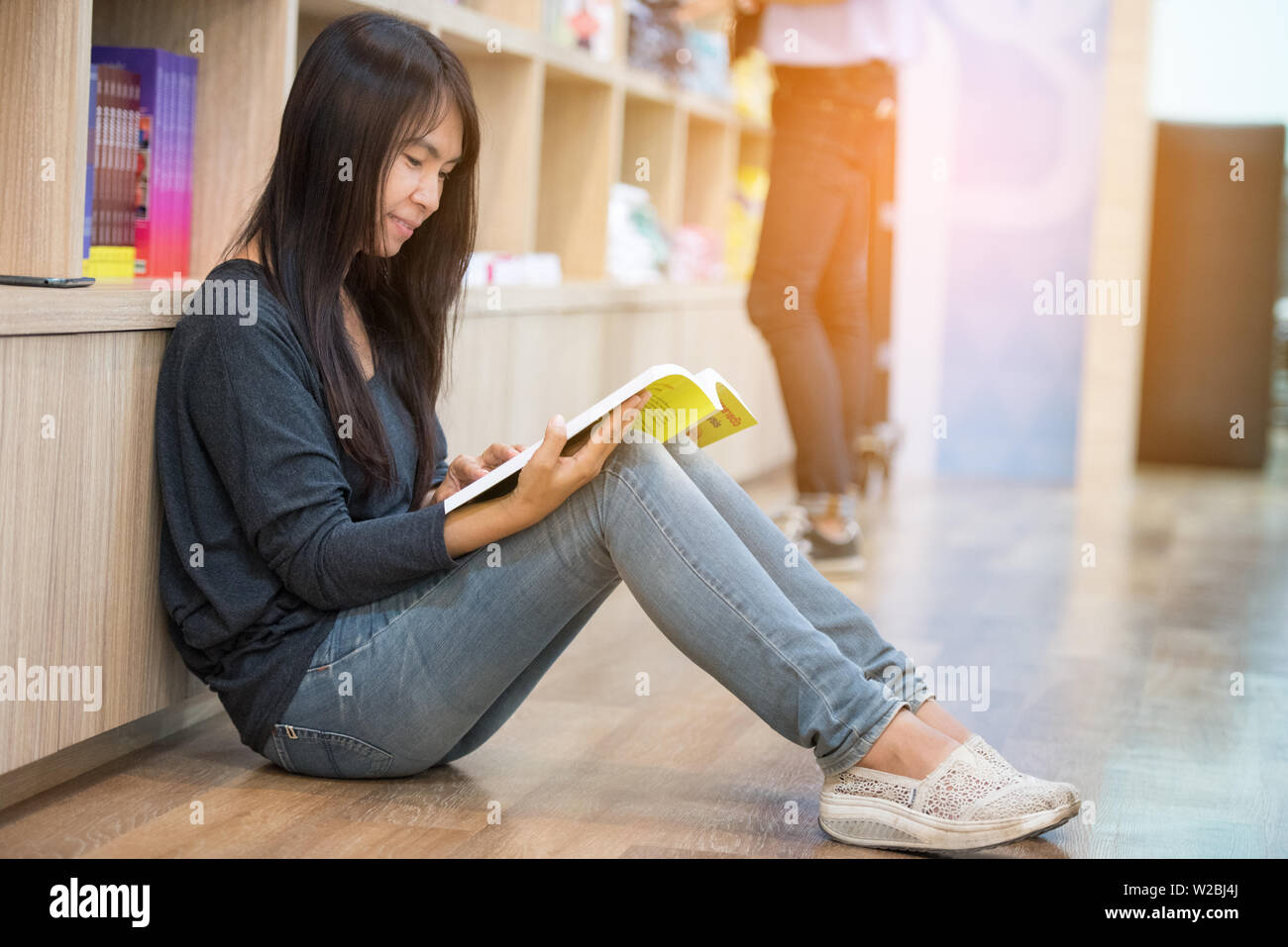 Junge schöne Frau mit Buch beim Sitzen auf dem Boden in der Bibliothek Stockfoto