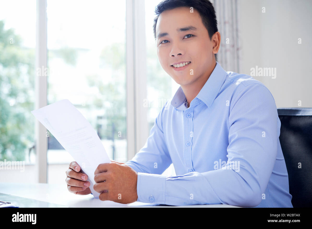 Portrait von gutaussehenden jungen asiatischen Geschäftsmann mit dem Dokument in der Hand am Tisch sitzen Stockfoto