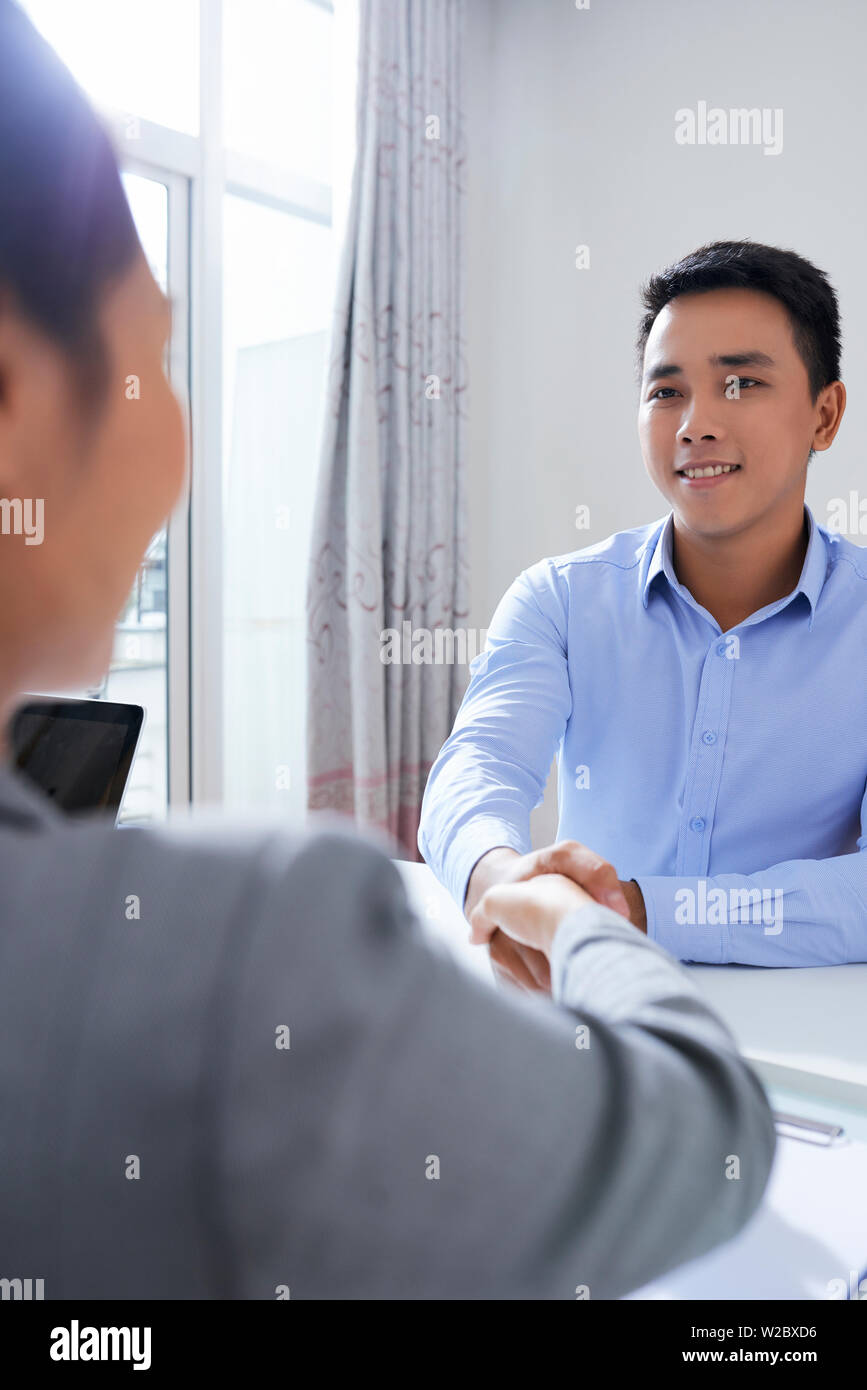 Fröhlichen jungen vietnamesischen Mann zitternden Hand der HR-Manager nach dem erfolgreichen Vorstellungsgespräch Stockfoto