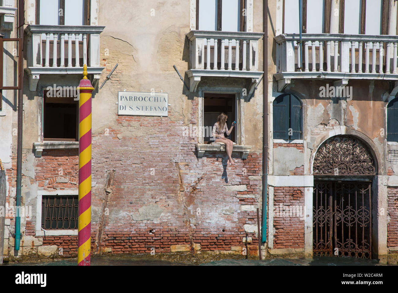 Junge Frau, die durch ein Fenster in einem Gebäude am Canale Grande, Venedig, Italien sitzen Stockfoto