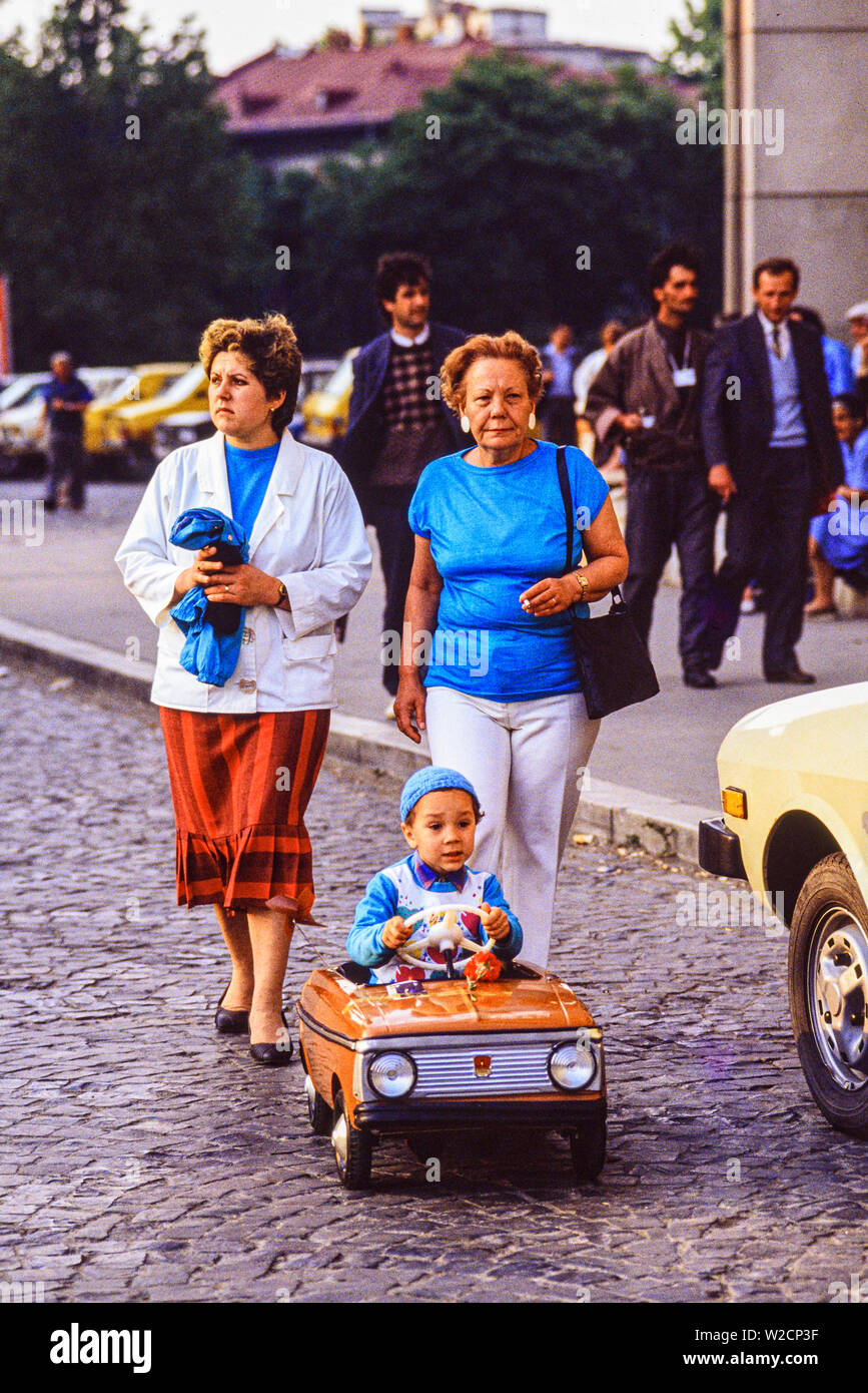 Bukarest, Rumänien. Mai 1990. Zwei Frauen zu Fuß hinter einem Kind in ein Spielzeugauto. Foto: © Simon Grosset. Archiv: Bild von einem ursprünglichen Transparenz digitalisiert. Stockfoto