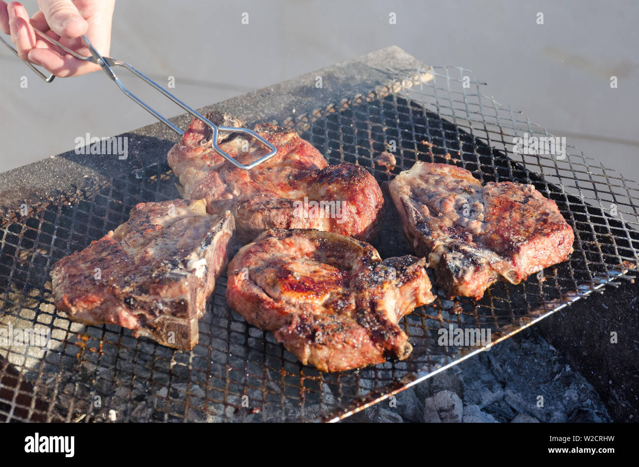 Hand mit der Zange ein rötliches Fleisch Steak auf dem Grill Gitter. Top Seitenansicht Stockfoto