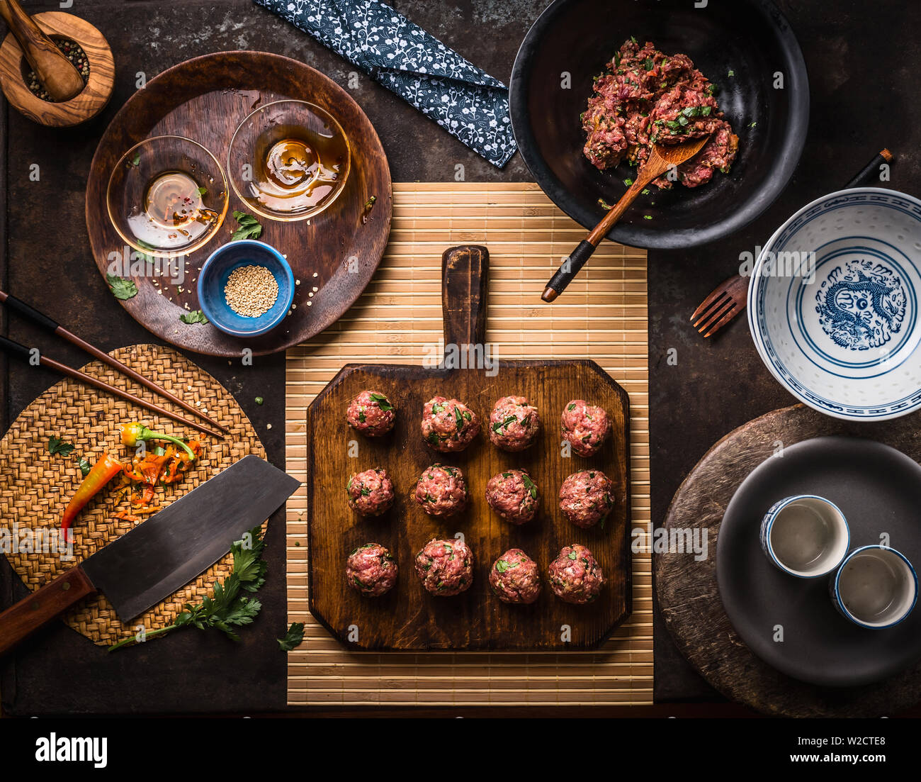 Asiatische Fleischbällchen auf Holz Schneidebrett mit Zutaten, Küchengeräte, Schüsseln und Teller, Ansicht von oben. Asiatische Küche Konzept Stockfoto