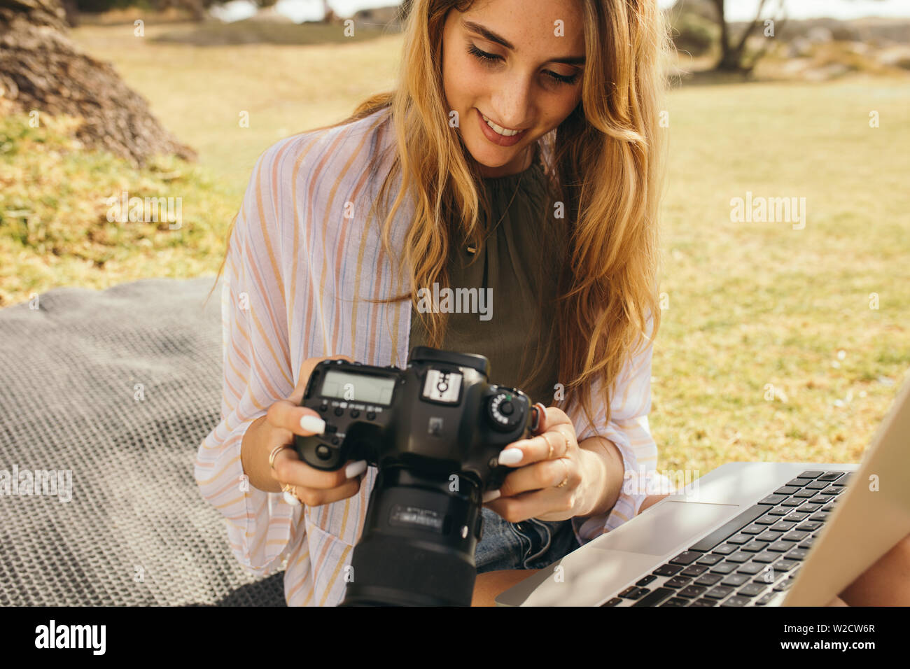 Nahaufnahme einer Frau Fotograf Sitzen im Freien eine DSLR-Kamera und Laptop. Lächelnde Frau Travel Blogger arbeiten an ihren Fotografien o Stockfoto