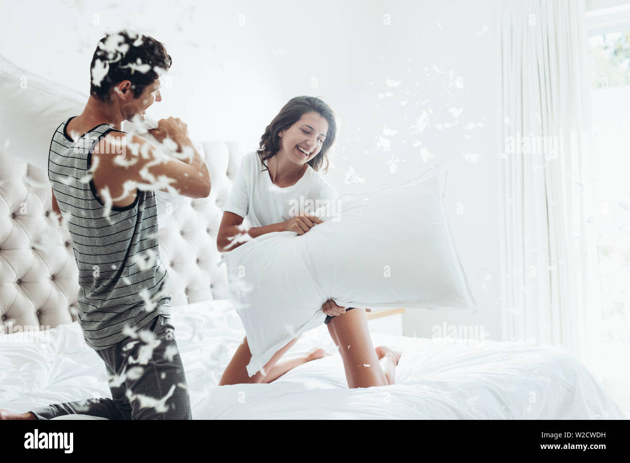 Junges Paar mit einer Kissenschlacht in Ihrem Schlafzimmer. Mann und Frau im Kampf mit Kissen auf dem Bett. Stockfoto
