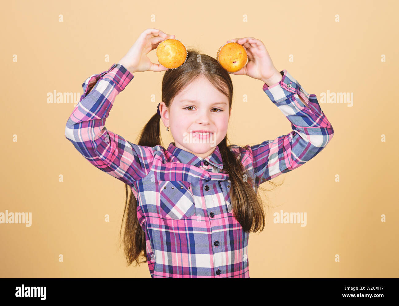 Genießen Sie ihr Liebling muffin Flavour. Happy little Girl holding Frühstück Muffins am Kopf. Kleines Kind glücklich lächelnd mit quickbread Muffins. Richtig testen jeden muffin Rezept. Stockfoto