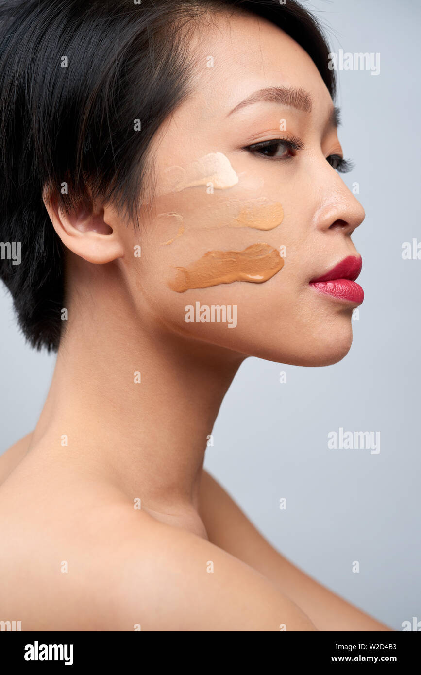 Seitenansicht des Asiatischen junge Frau mit dunklen kurzen Haaren in verschiedenen Farben der Stiftung für Gesichts-Make-up Stockfoto