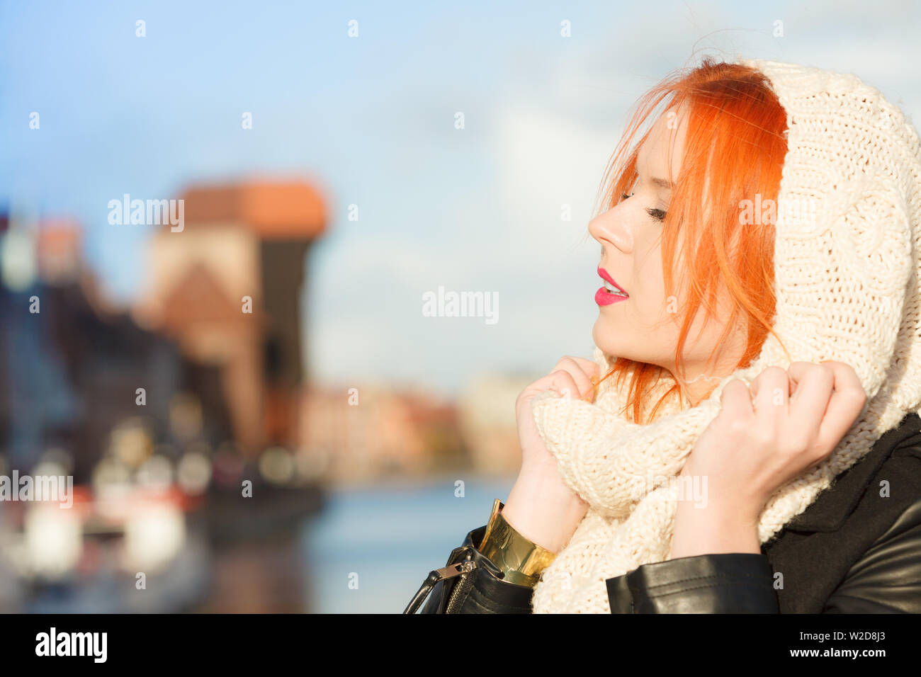 Winter Fashion. Beauty girl portrait rote Haare junge Frau in warme Kleidung im Freien genießen Sonnenlicht an einem sonnigen Tag. Stadt Danzig im Hintergrund Stockfoto