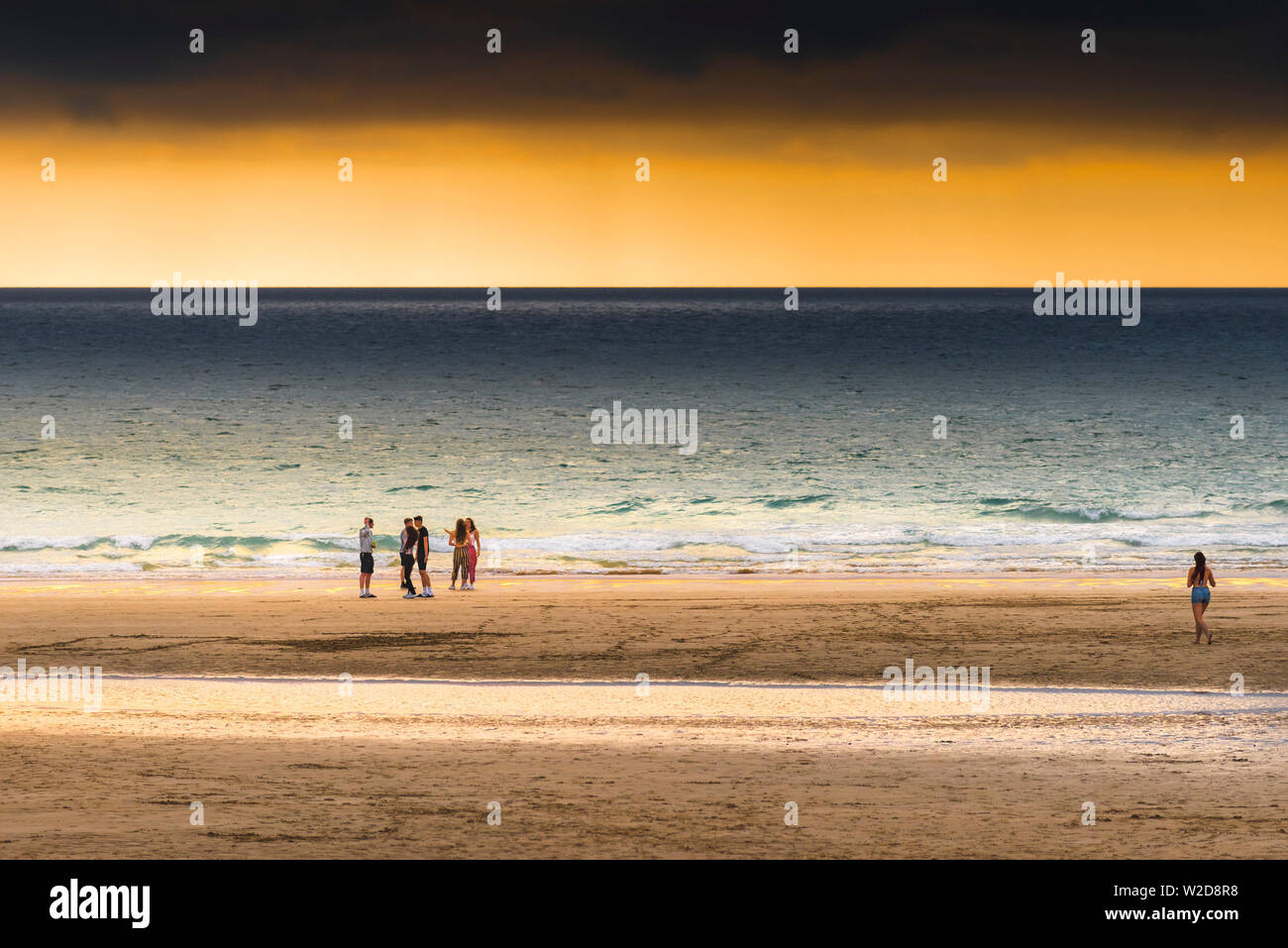 Eine Gruppe von Jugendlichen heraus hängen auf den Fistral Beach in einer dramatischen Sonnenuntergang in Newquay in Cornwall. Stockfoto