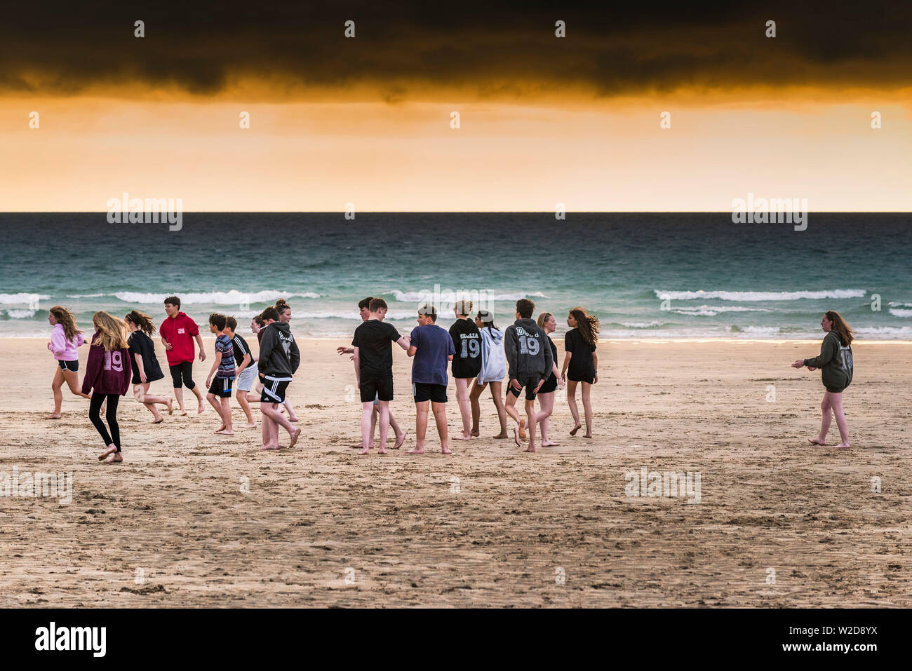 Eine Gruppe von Jugendlichen heraus hängen auf den Fistral Beach in einer dramatischen Sonnenuntergang in Newquay in Cornwall. Stockfoto