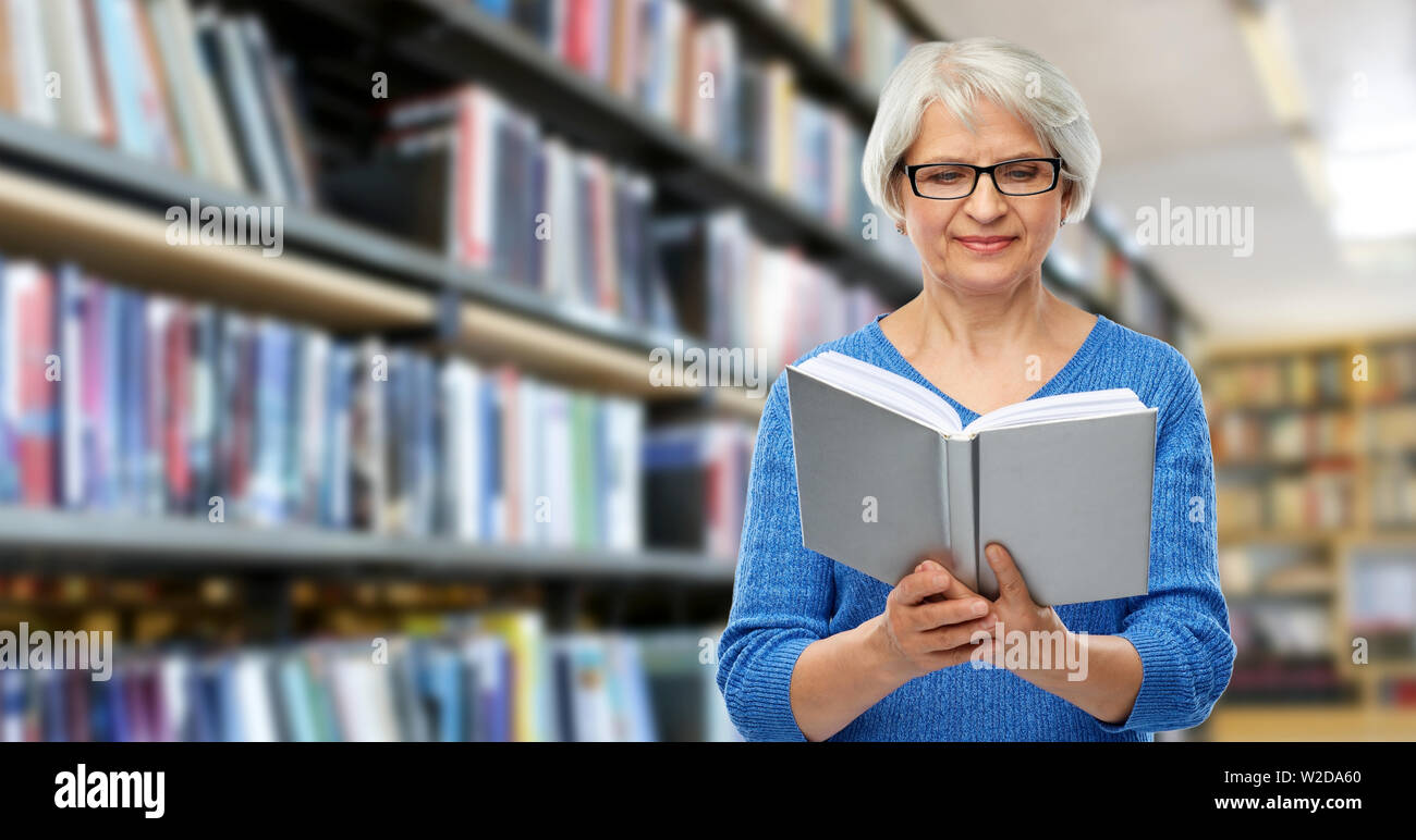 Ältere Frau in Gläser Buch an der Bibliothek Stockfoto