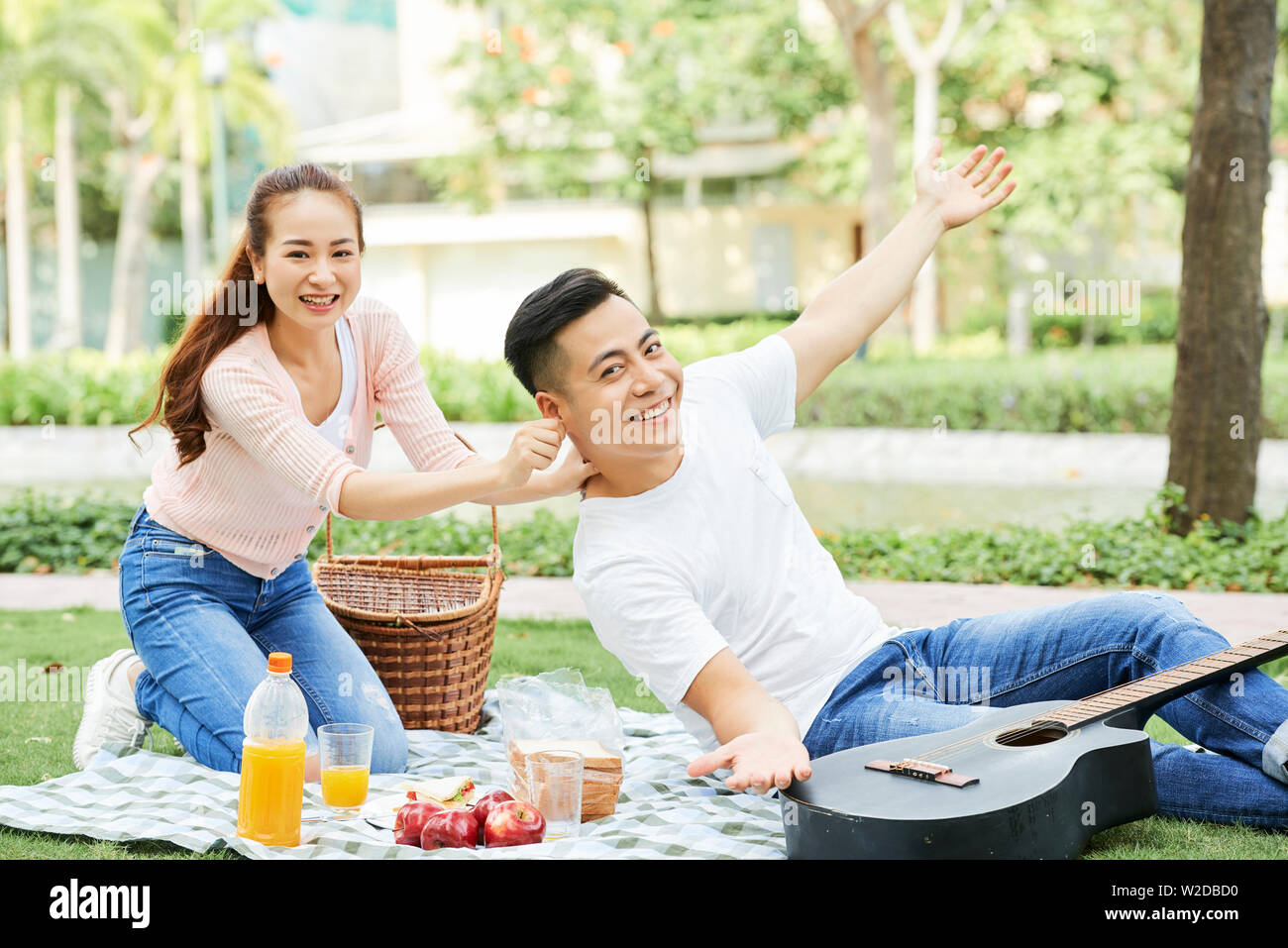 Portrait von glücklichen jungen asiatischen Paar lächelnd an Kamera und dabei Spaß haben während ihrer Picknick im Park Stockfoto