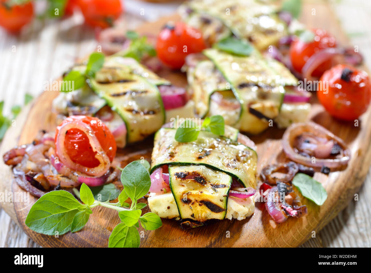 Vegetarisch grillen Mahlzeit: Gegrilltes griechischer Schafskäse mit roten Zwiebeln in dünne Zucchinischeiben gewickelt, mit hot Cherry Tomaten serviert. Stockfoto