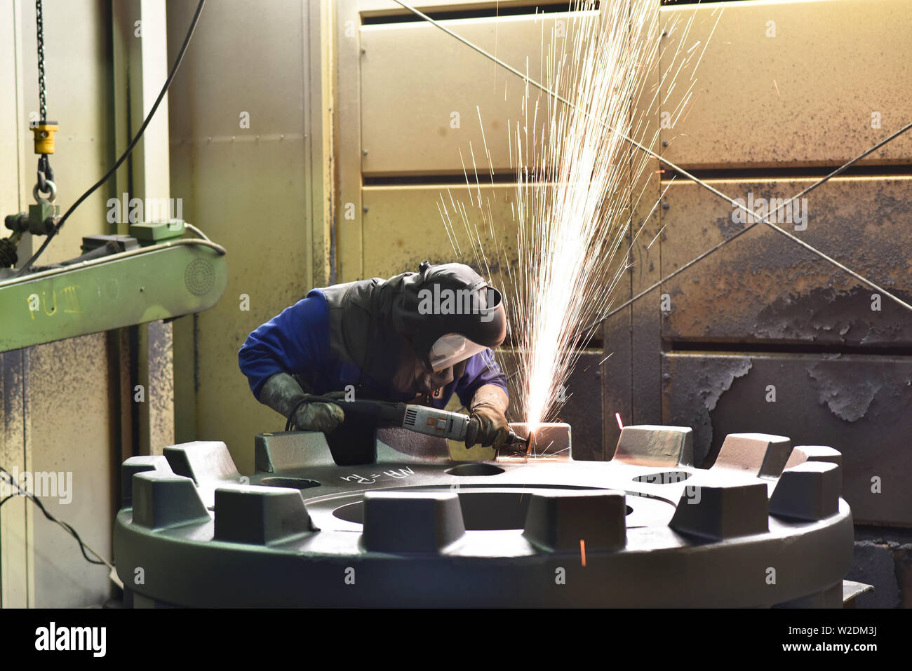 Arbeiter in Schutzkleidung in einer Gießerei arbeiten an einem Casting mit Schleifmaschine am Arbeitsplatz Stockfoto