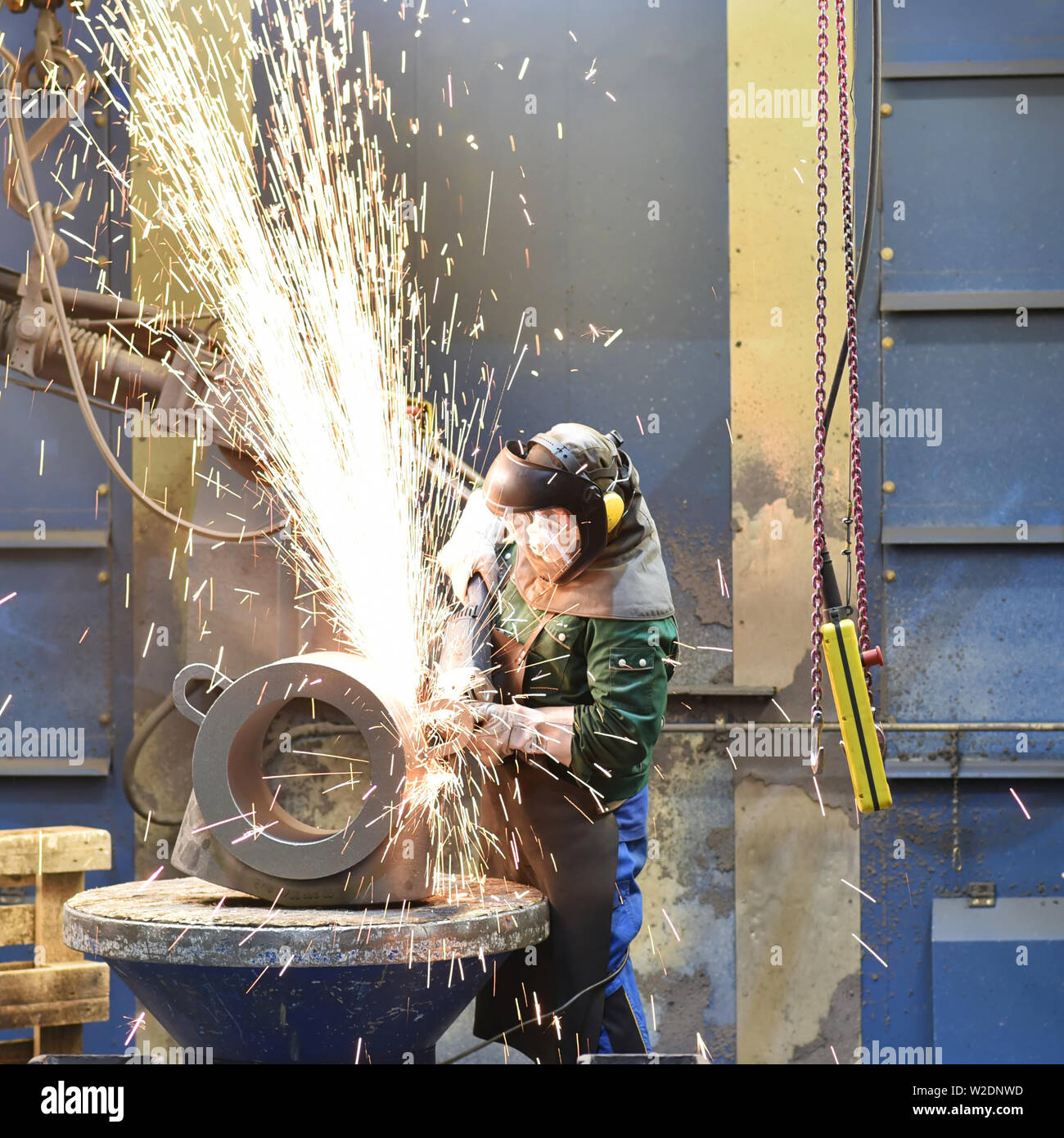 Arbeiter in Schutzkleidung in einer Gießerei arbeiten an einem Casting mit Schleifmaschine am Arbeitsplatz Stockfoto