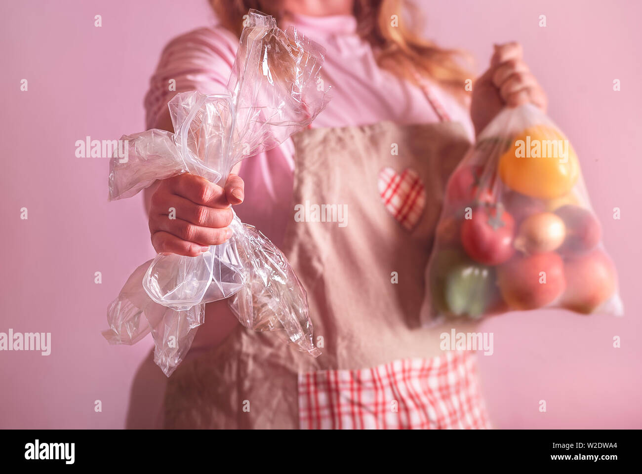 Null Abfall, kein Plastik Konzept, mit einer Frau, die die Lebensmittel in einem umweltfreundlichen wiederverwendbaren Netzbeutel und in der einen Hand die leere Plastikverpackungen. Stockfoto