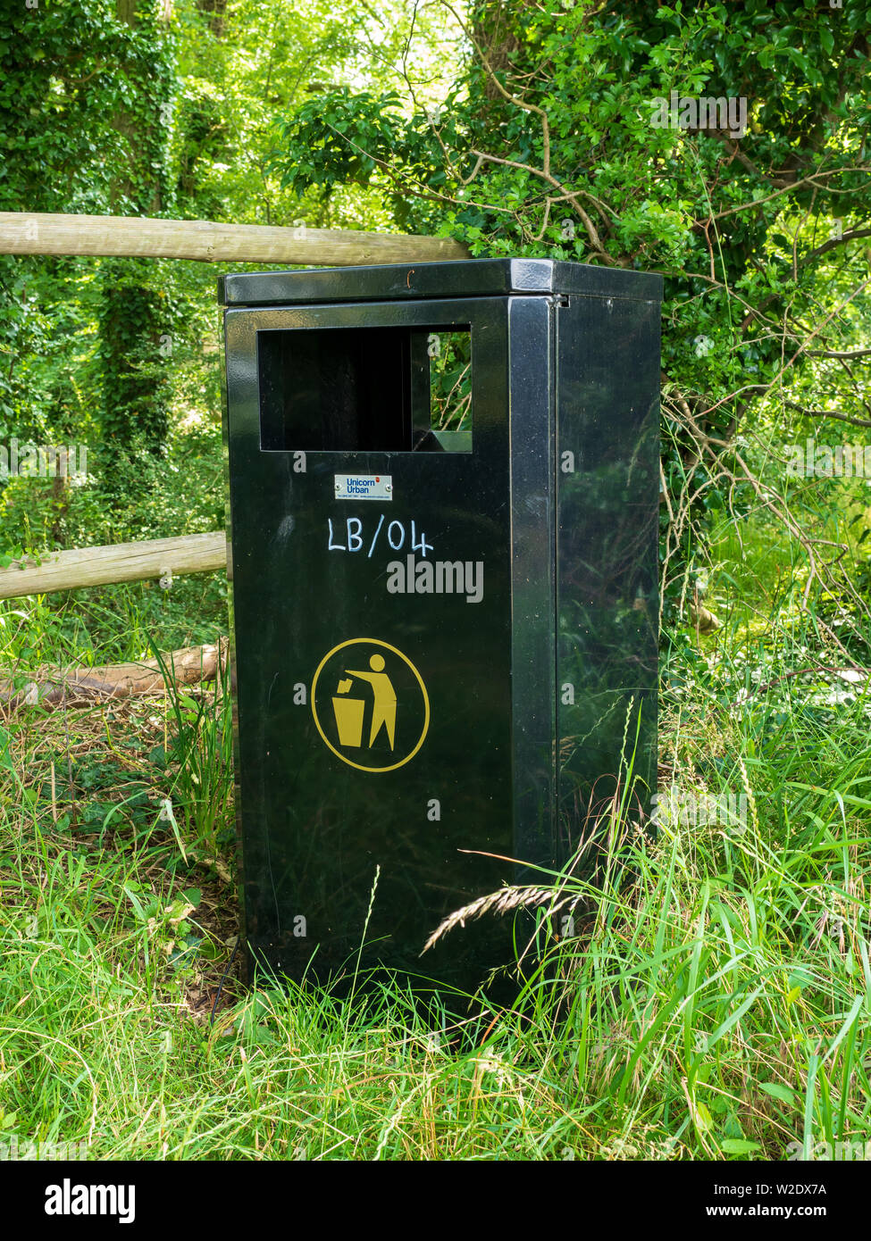 Grüner Metallmüllbehälter, der vom rat neben einem zur Verfügung gestellt wird Öffentlicher Fußweg im Wald, um die Menschen zu ermutigen, nicht zu fallen Wurf Stockfoto