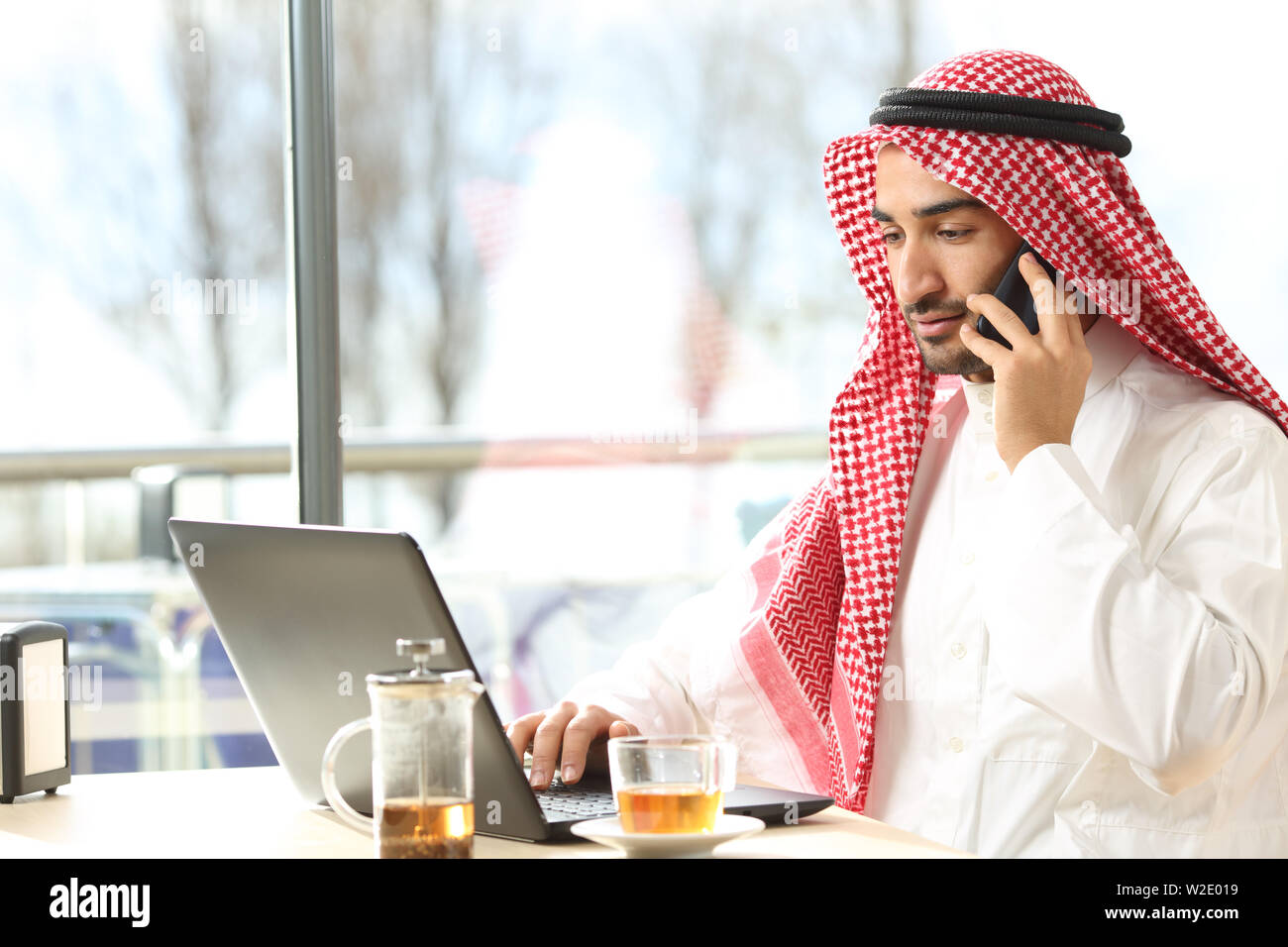 Arabischer Mann mit einem Laptop und dem Sprechen für snmart Telefon in einem Café sitzen Stockfoto