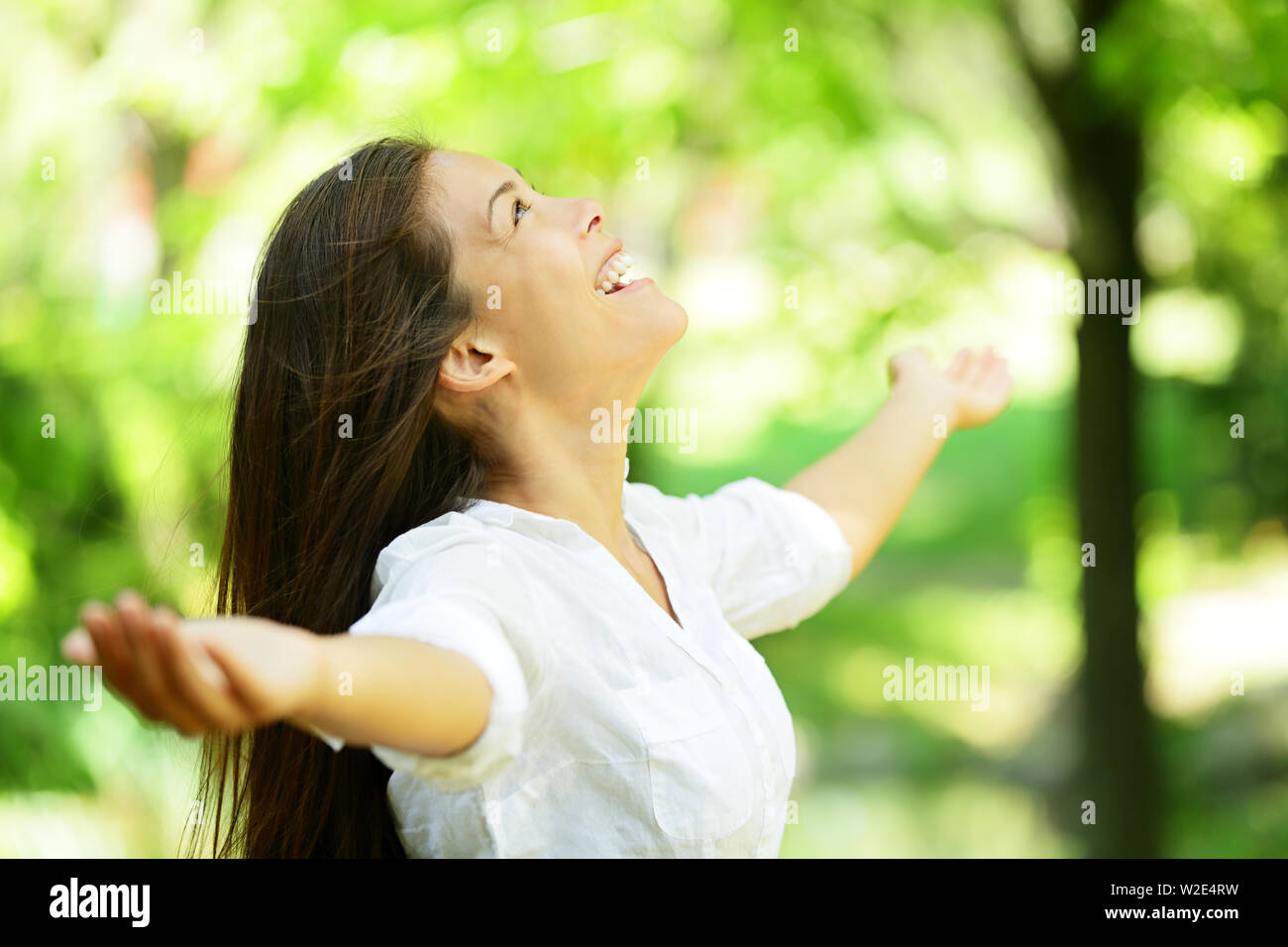 Attraktive junge Frau im Frühjahr oder Sommer Garten seitlich stehend, die Arme ausgestreckt und erfreuen Sie Ihren Kopf in den Himmel genießen die Frische und die Schönheit der Natur angehoben Stockfoto