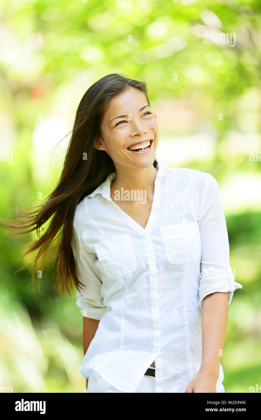Fröhliche temperamentvolle Frau im Frühjahr oder Sommer Park strahlt ein breites Lächeln, als sie Wanderungen entlang der Freude in der Frische der Natur und das warme Glühen des Sonnenlichtes durch die Blätter der grünen Bäumen, Stockfoto