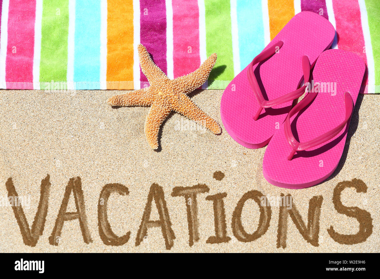 Ferienhäuser Strand reisen text Konzept. Ferien in Sand geschrieben mit Wasser neben Strandtuch, Sommer Sandalen und Seesterne. Sommer und Sonne Urlaub Ferien. Stockfoto