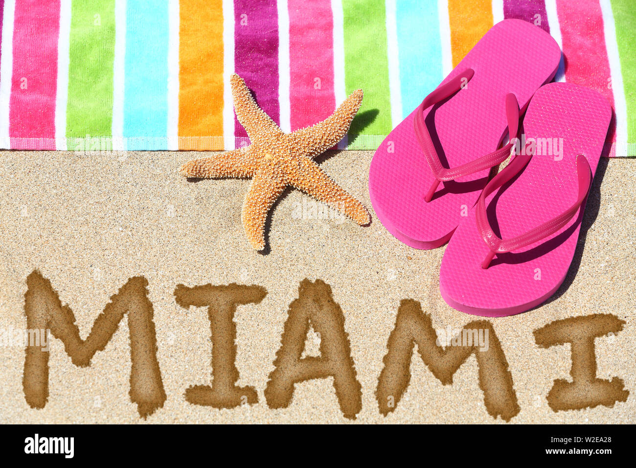 Miami, Florida Beach Travel Concept. MIAMI in Sand geschrieben mit Wasser neben Strandtuch, Sommer Sandalen und Seesterne. Sommer und Sonne Urlaub Ferien. Stockfoto