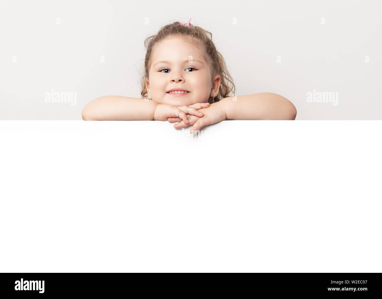 Lächelnd blue eyed kleines Mädchen spähen hinter einer weißen Tafel. Stockfoto