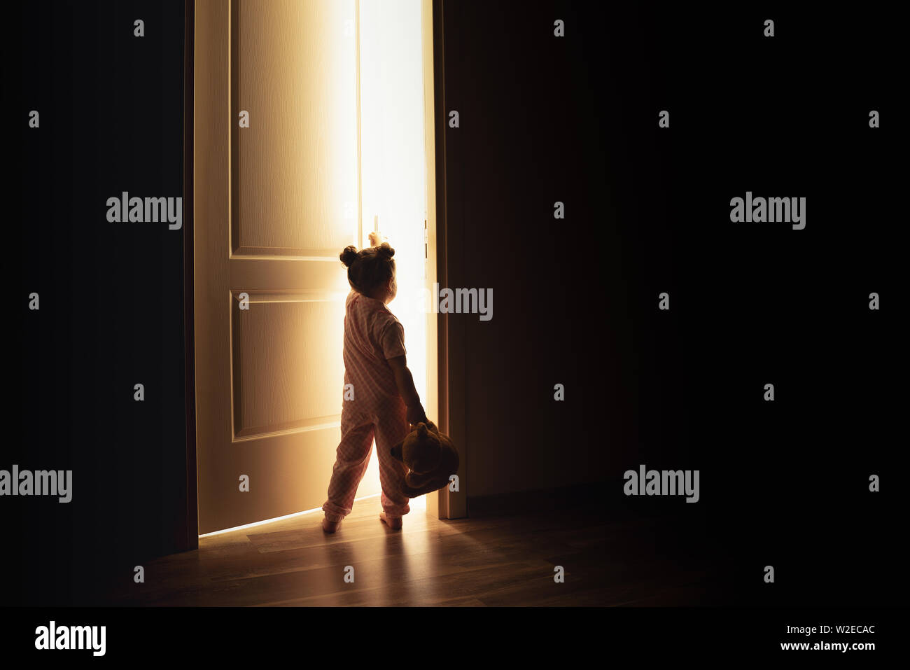 Kleines Mädchen öffnet die Tür zum Licht in der Dunkelheit. Stockfoto