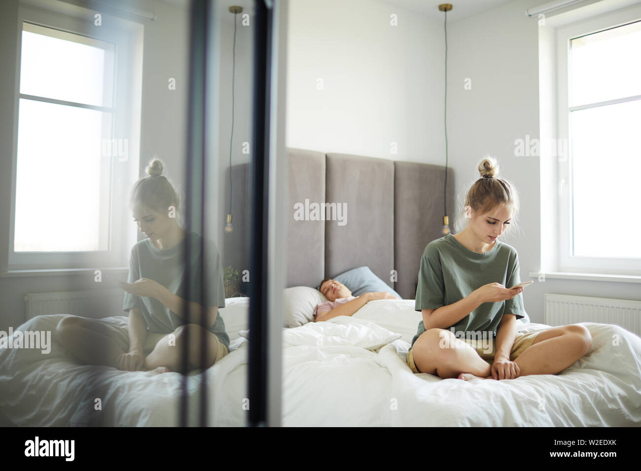 Junge Frau sitzt auf dem Bett und schauen durch Nachrichten in ihrem Ehemann smartphone Stockfoto