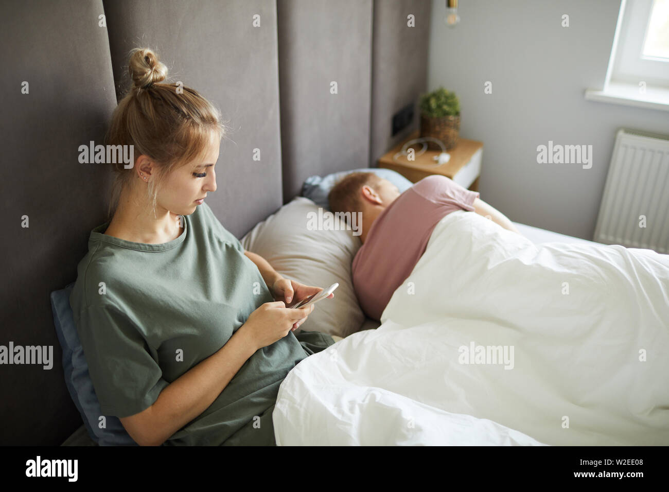 Verdächtige junge Frau Blättern in ihrem Ehemann Smartphone, während Sie im Bett sitzen Stockfoto