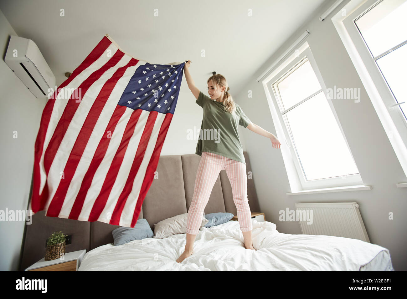 Hübsche Frau in der casualwear auf Bett und wehende Amerikanische Flagge während der Feier des nationalen Tag der Unabhängigkeit Stockfoto